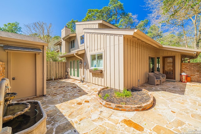 back of property featuring board and batten siding, fence, french doors, a chimney, and a patio