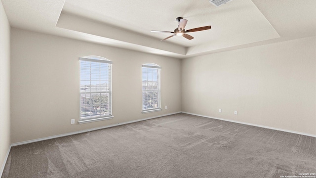 unfurnished room featuring carpet, a raised ceiling, a ceiling fan, and baseboards