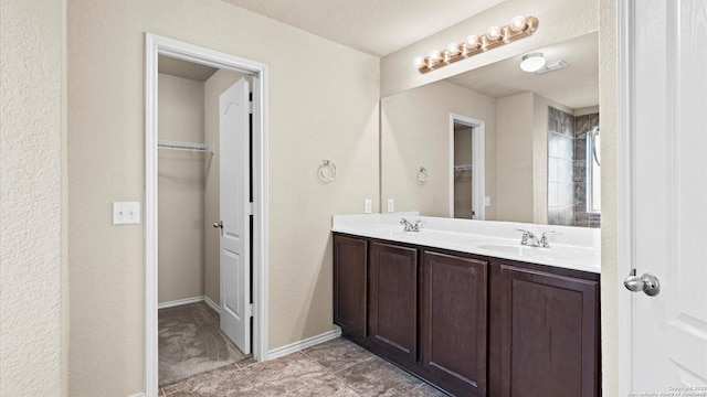 bathroom featuring double vanity, a spacious closet, baseboards, and a sink