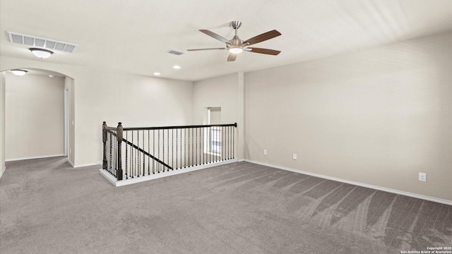 carpeted spare room featuring arched walkways, visible vents, baseboards, and ceiling fan