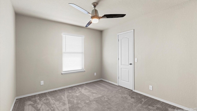 carpeted spare room featuring baseboards and a ceiling fan