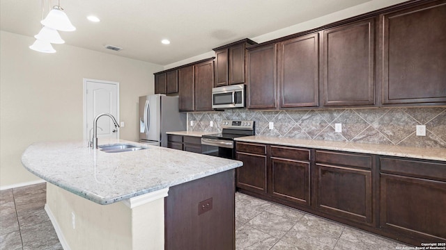 kitchen featuring visible vents, a center island with sink, a sink, backsplash, and appliances with stainless steel finishes