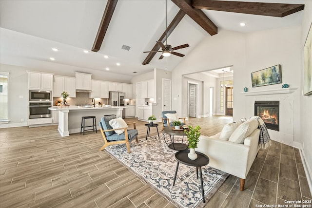 living area featuring a ceiling fan, visible vents, wood finish floors, beam ceiling, and a tile fireplace