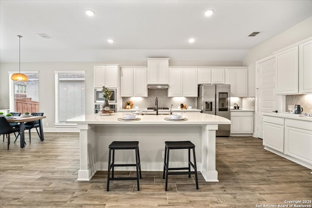 kitchen with an island with sink, under cabinet range hood, white cabinetry, appliances with stainless steel finishes, and a breakfast bar area