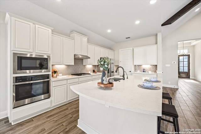 kitchen featuring oven, built in microwave, lofted ceiling, gas stovetop, and a sink