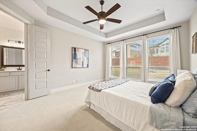 carpeted bedroom featuring ensuite bath, baseboards, a tray ceiling, and a sink