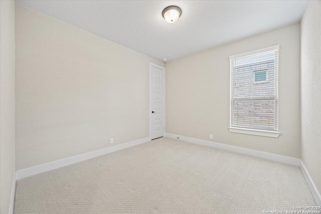 spare room featuring baseboards, light colored carpet, and a textured ceiling