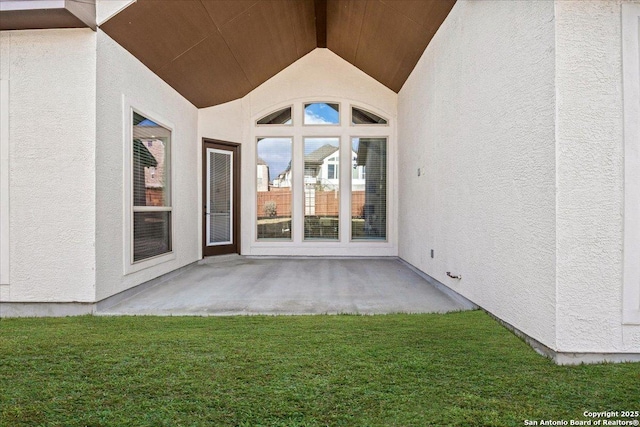 entrance to property with a patio area, stucco siding, and a lawn