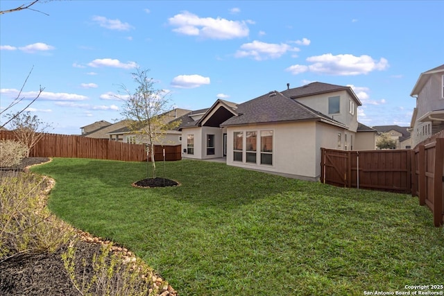 rear view of house with stucco siding, a yard, roof with shingles, and a fenced backyard