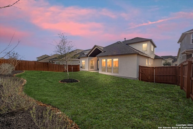 rear view of house with a yard, a shingled roof, a fenced backyard, and stucco siding