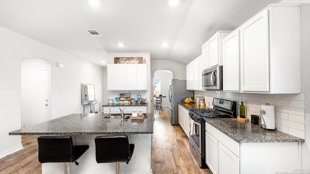 kitchen with visible vents, a kitchen island with sink, arched walkways, stainless steel appliances, and vaulted ceiling