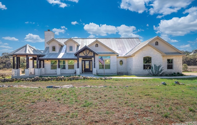 view of front of house featuring a front lawn, a chimney, metal roof, stone siding, and a standing seam roof