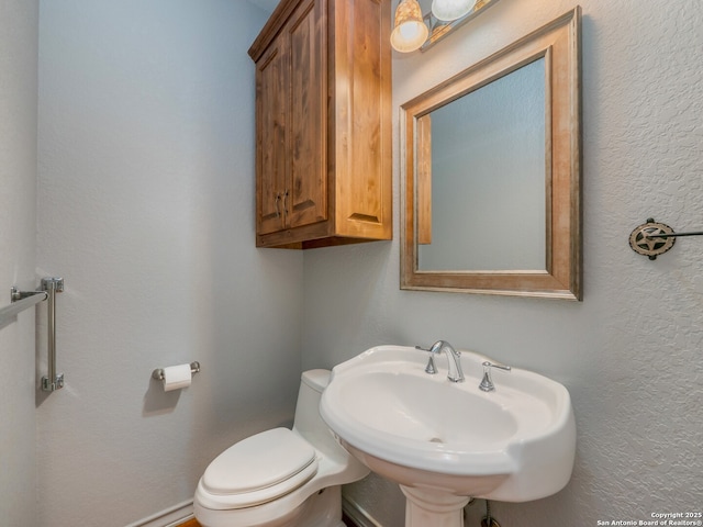 half bath with a sink, toilet, and a textured wall