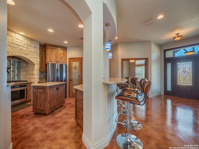 kitchen featuring light countertops, arched walkways, brown cabinets, and stainless steel appliances