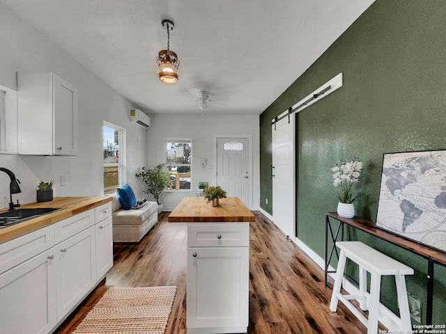 kitchen with a ceiling fan, a sink, a barn door, white cabinets, and butcher block counters