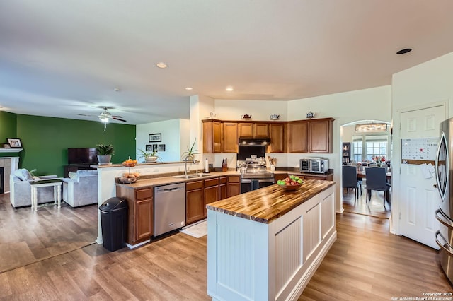 kitchen featuring light wood-style flooring, open floor plan, stainless steel appliances, brown cabinetry, and butcher block counters