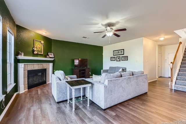 living area featuring visible vents, wood finished floors, stairway, a fireplace, and ceiling fan