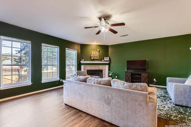 living area with visible vents, a wealth of natural light, a fireplace, wood finished floors, and a ceiling fan