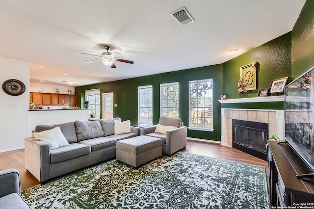 living area with visible vents, plenty of natural light, wood finished floors, and a ceiling fan