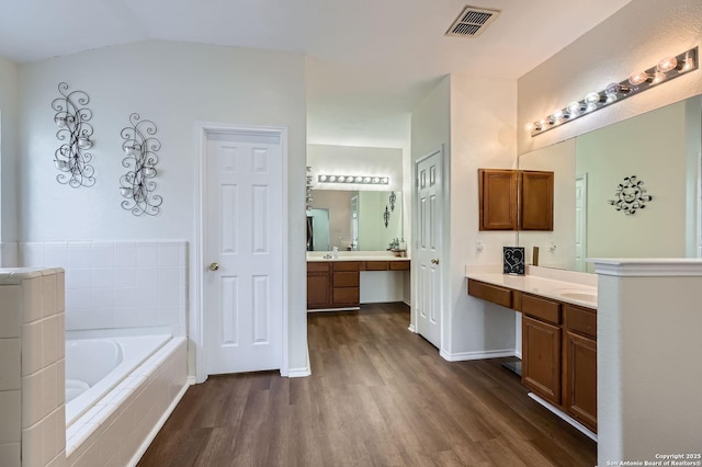 full bathroom with a garden tub, two vanities, wood finished floors, and visible vents