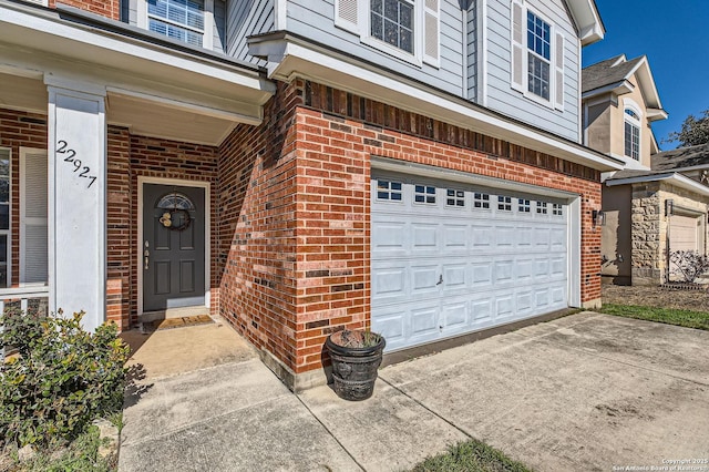 property entrance featuring brick siding, concrete driveway, and an attached garage