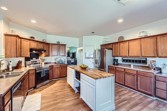 kitchen with light wood finished floors, butcher block countertops, a sink, under cabinet range hood, and appliances with stainless steel finishes