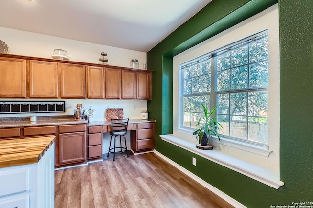 kitchen with brown cabinetry, light wood-style flooring, butcher block countertops, and built in study area