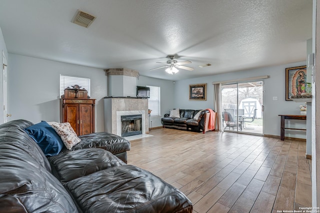 living room featuring light wood finished floors, visible vents, a textured ceiling, and ceiling fan