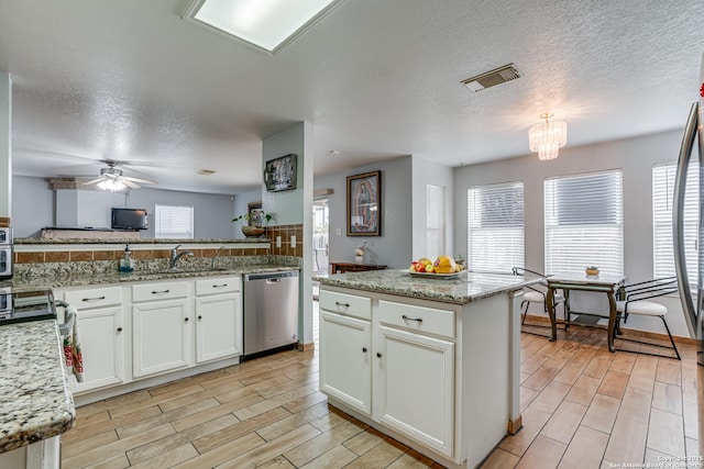 kitchen featuring a wealth of natural light, visible vents, stainless steel dishwasher, and ceiling fan with notable chandelier