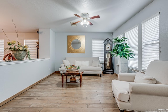 living room with ceiling fan, visible vents, baseboards, and light wood-style flooring