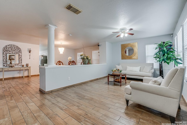 living area featuring visible vents, a ceiling fan, light wood-style floors, and ornate columns