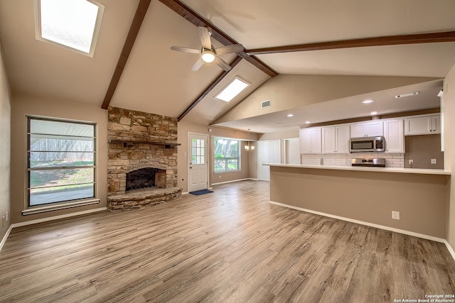 unfurnished living room with ceiling fan, beamed ceiling, a stone fireplace, light wood-style flooring, and high vaulted ceiling