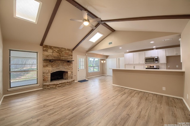 unfurnished living room featuring high vaulted ceiling, beam ceiling, ceiling fan, a stone fireplace, and light wood-style floors