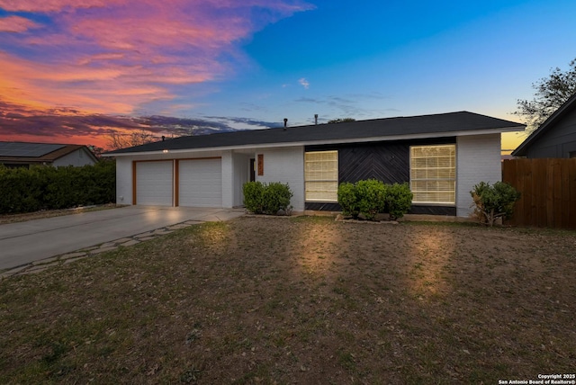 view of front of house featuring brick siding, fence, concrete driveway, a lawn, and an attached garage