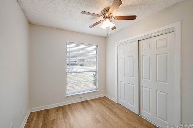 unfurnished bedroom with baseboards, light wood finished floors, ceiling fan, a closet, and a textured ceiling