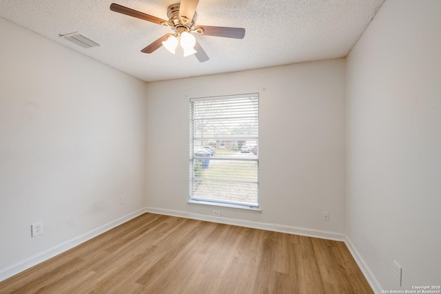 empty room featuring light wood-type flooring, visible vents, baseboards, and a textured ceiling