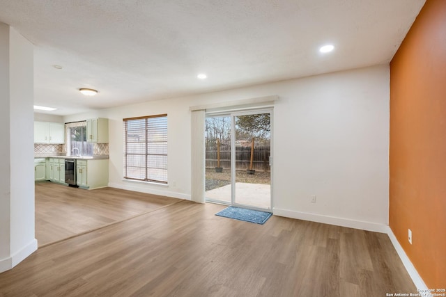 unfurnished living room featuring beverage cooler, recessed lighting, baseboards, and light wood-style floors