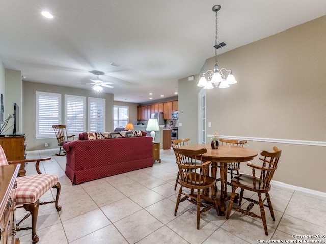 dining space with a wealth of natural light, ceiling fan with notable chandelier, baseboards, and light tile patterned flooring