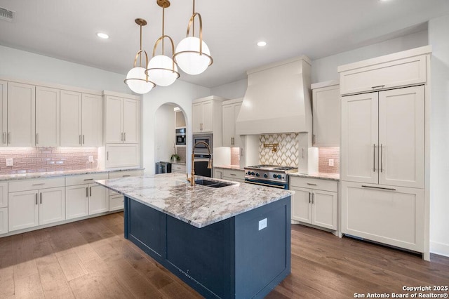 kitchen featuring dark wood-style flooring, arched walkways, custom range hood, white cabinets, and appliances with stainless steel finishes