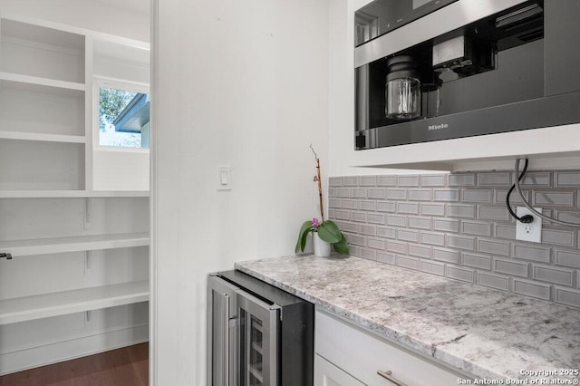 kitchen with tasteful backsplash, light stone countertops, wine cooler, wood finished floors, and white cabinetry