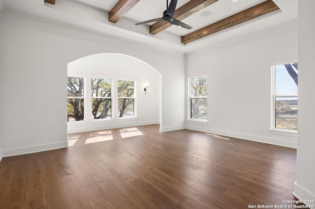 unfurnished room featuring baseboards, ceiling fan, beamed ceiling, arched walkways, and wood-type flooring