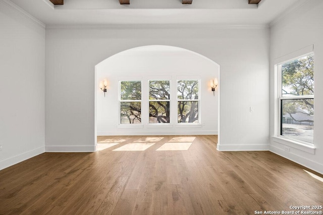 empty room featuring ornamental molding, wood finished floors, arched walkways, and baseboards