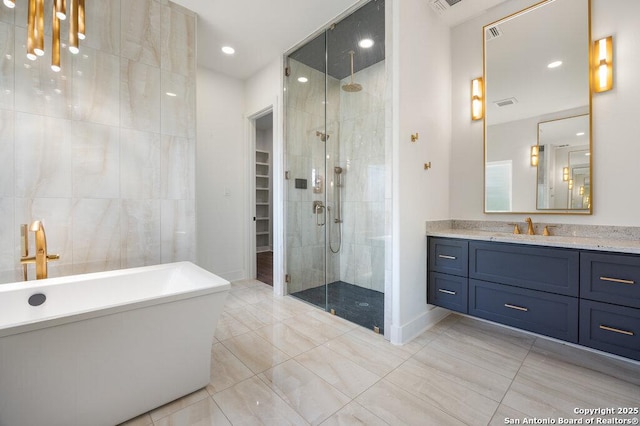 full bath featuring a walk in closet, tile walls, a shower stall, a freestanding bath, and vanity