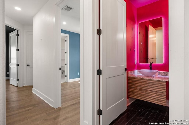 hall with baseboards, wood finished floors, visible vents, and a sink