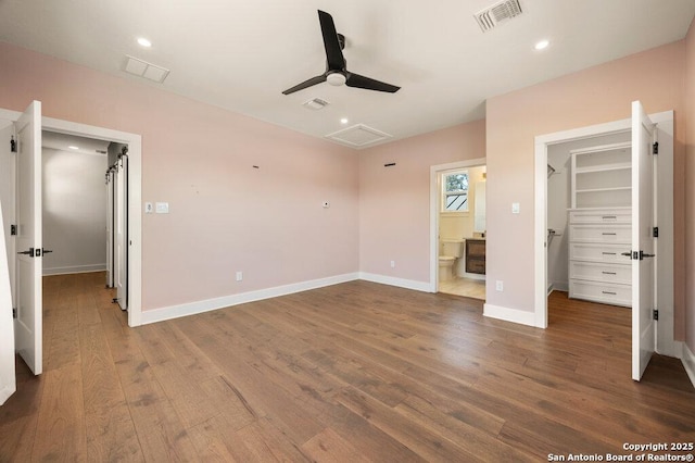 unfurnished bedroom with visible vents, a walk in closet, baseboards, recessed lighting, and wood finished floors