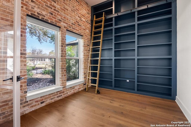 empty room with built in features, wood finished floors, and brick wall