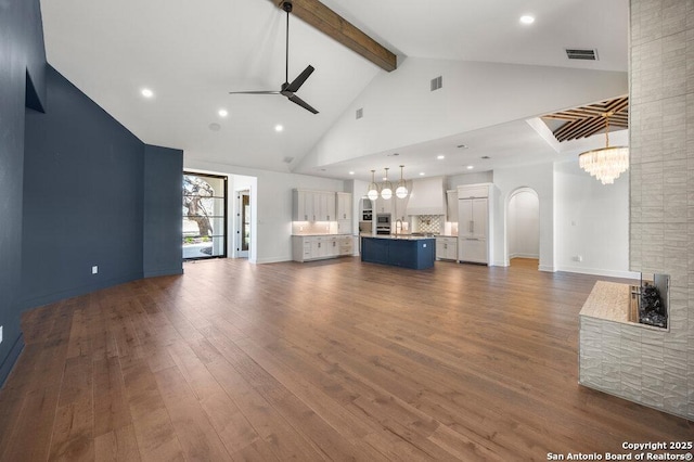 unfurnished living room featuring dark wood-style floors, visible vents, high vaulted ceiling, beam ceiling, and ceiling fan with notable chandelier