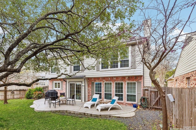 rear view of house featuring a yard, a patio area, brick siding, and a fenced backyard