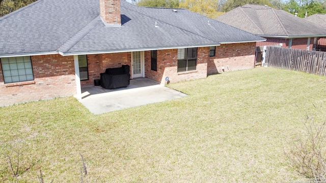 rear view of house featuring a lawn, a patio, fence, roof with shingles, and a chimney