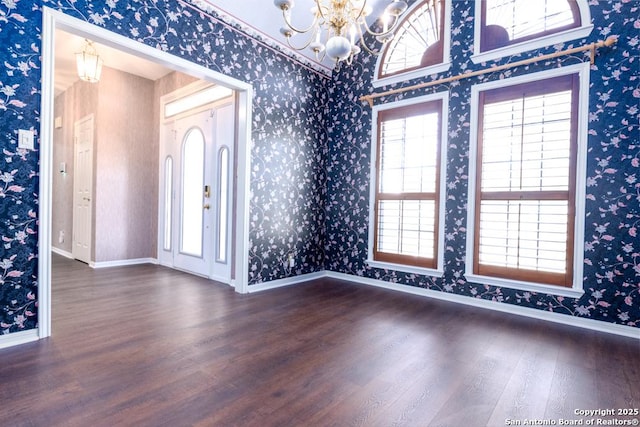 unfurnished room with baseboards, wallpapered walls, an inviting chandelier, and wood finished floors